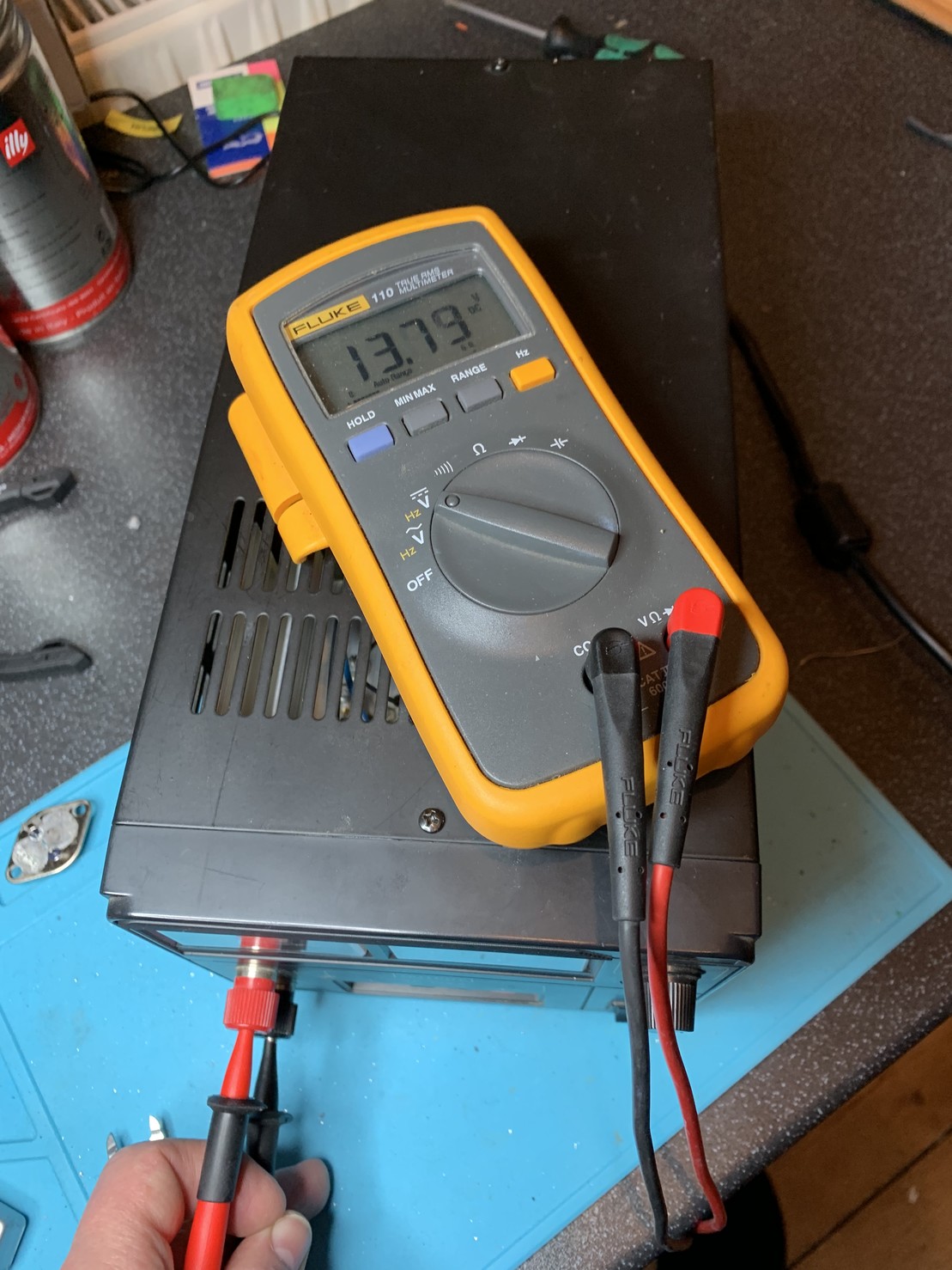 A multimeter plugged into a PSU. The voltage reads 13.79 Vdc