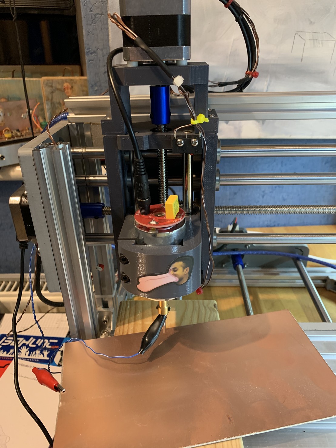 A wider view of the 3D printed z-axis of the machine. There’s a stepper motor at the top and a gantry holding a motor. The housing has a sticker of a man with a comically large tongue (it’s a friend of mine)