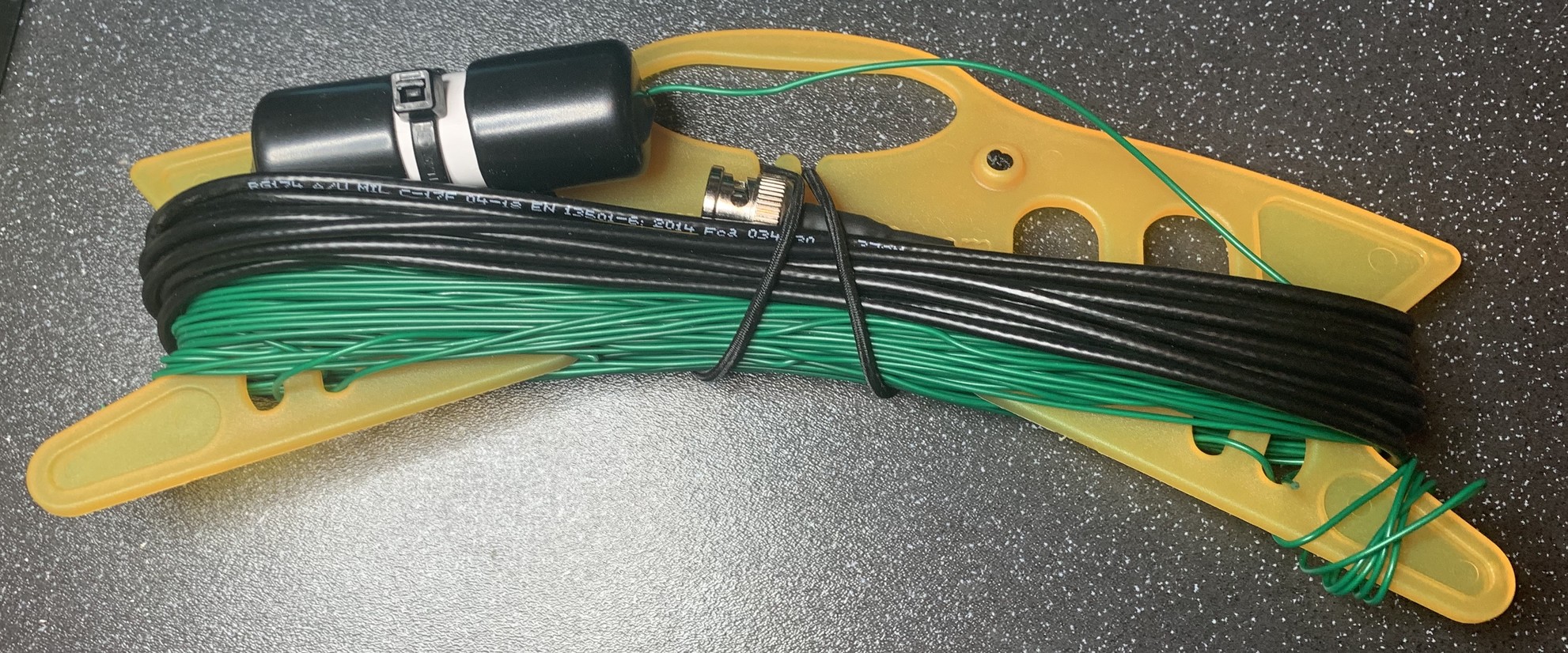 This shows a cable winder with some green antenna wire, some black feeder (a thin coax) and a small capsule of plastic pipe. The pipe contains a small tuned circuit. 