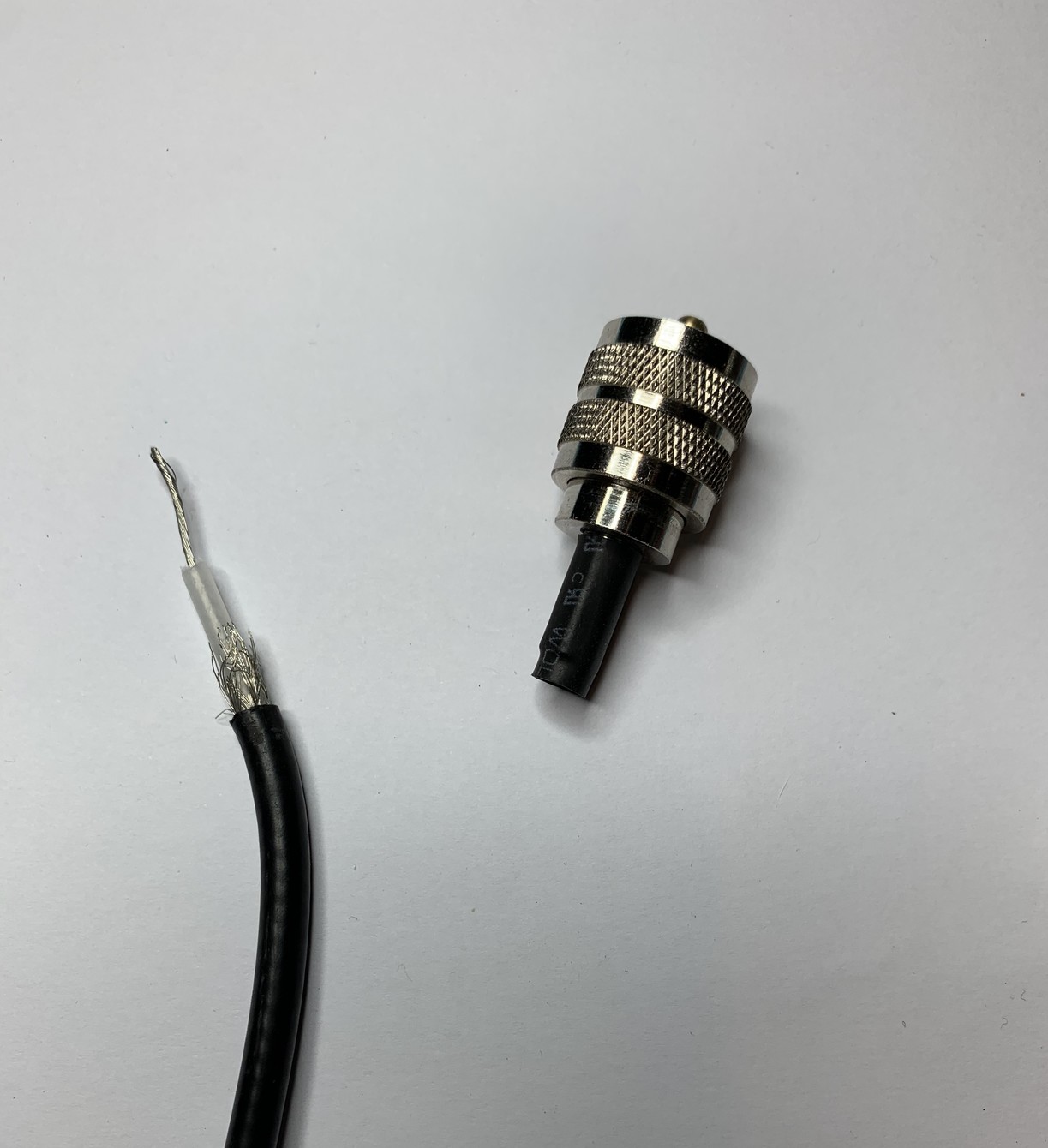 On the left is a section of coax cable. Stripped and with the braid showing. On the right is a PL-259 crimp plug which has a heat shrink tube still attached. The coax fell out as it wasn’t properly attached. 