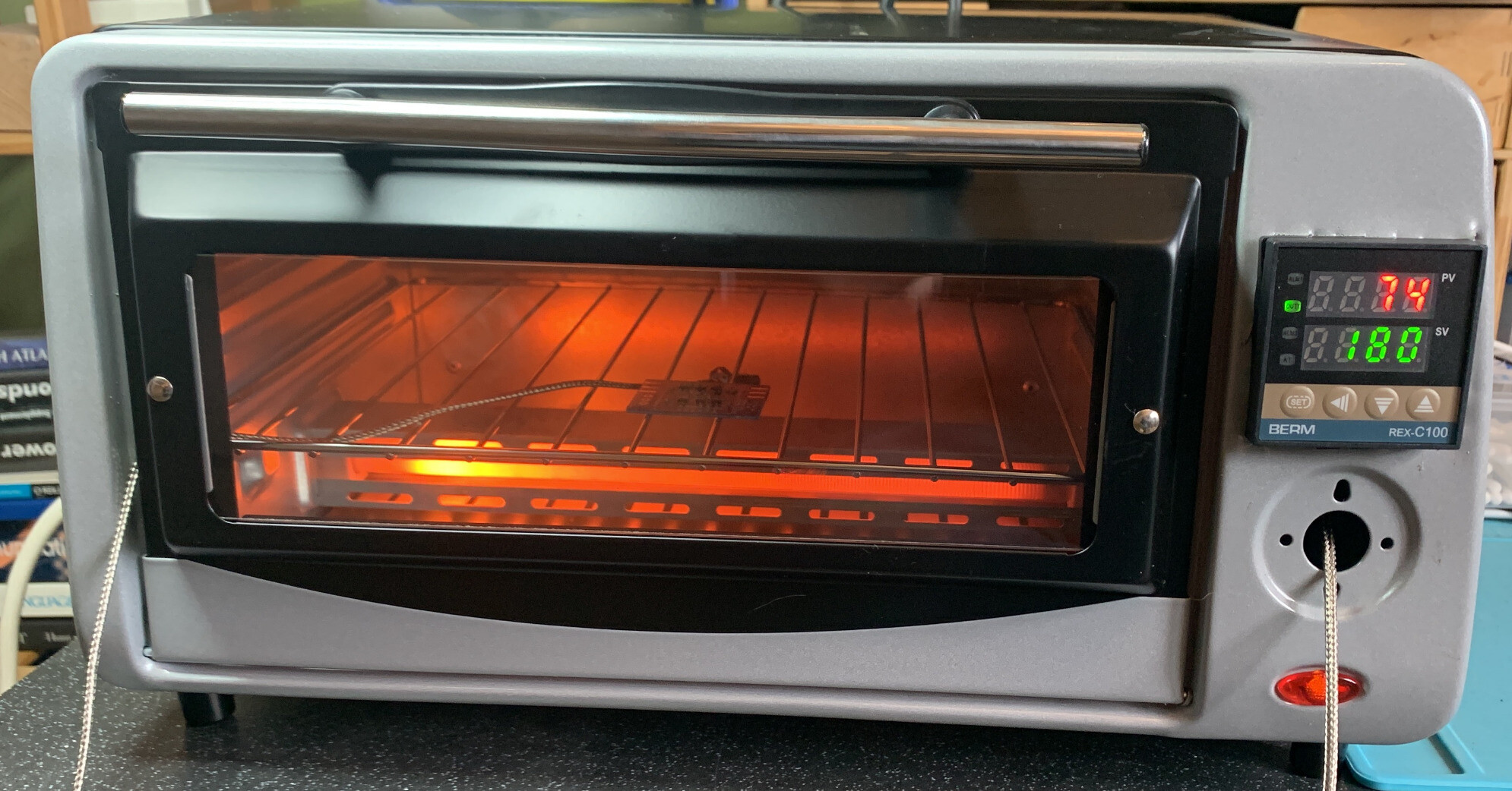 A modified toaster oven. There’s a controller on the right where the dials would be. It has two temperature readouts. Inside is a small PCB. There’s a metal wire going through the door. 